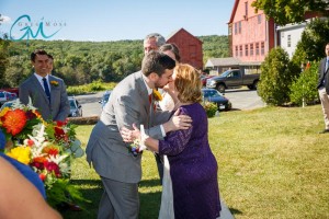 A bride and groom kiss, surrounded by guests and vibrant flowers, with a red barn in the background on a sunny day at Salem Cross Inn.