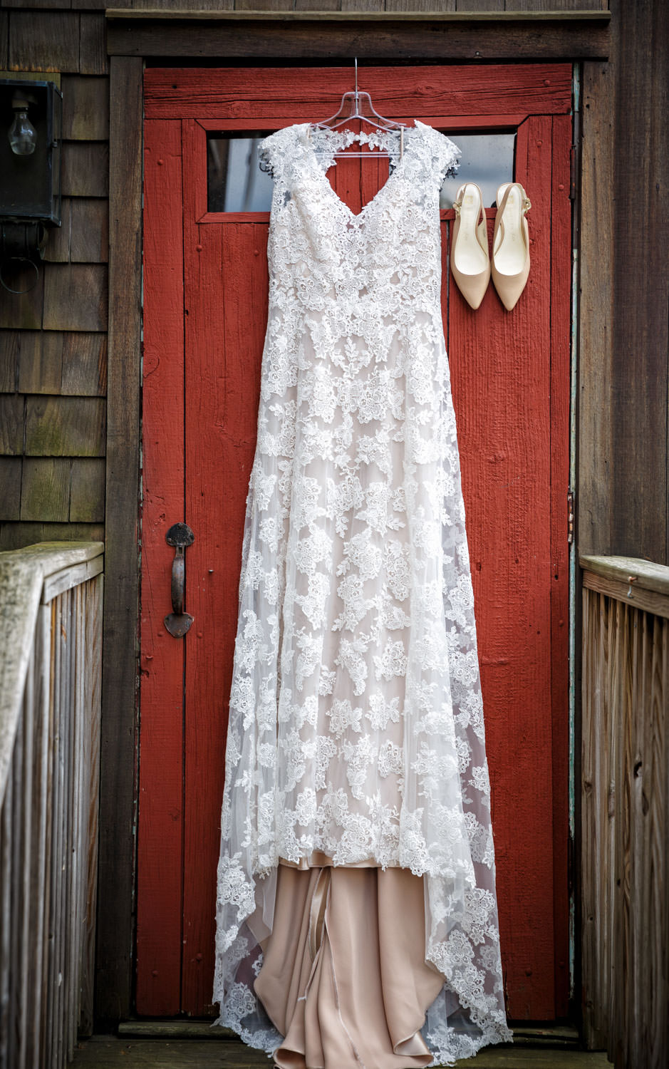 Brides wedding shoes and dress hanging outside on the red barn door at the Salem Cross Inn. This photo works well with the red of the door contrasting the brides off white dress.