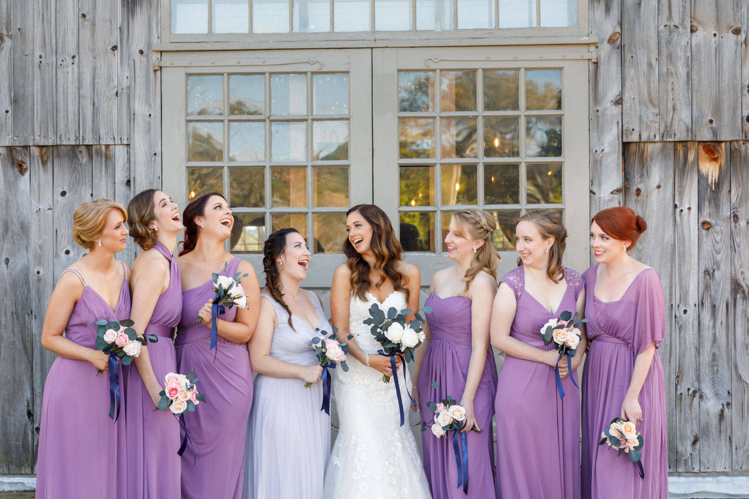 Bride with bridesmaids laughing in front of the barn.
