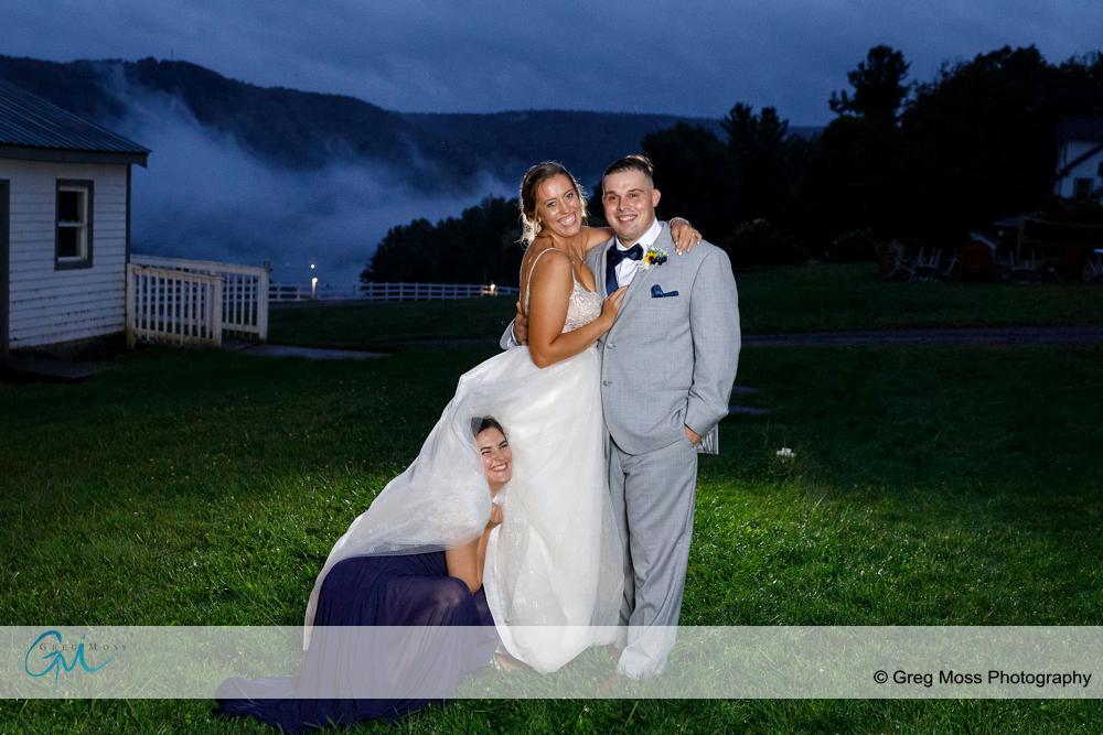 Bride and groom with maid of honor hiding in brides dress.