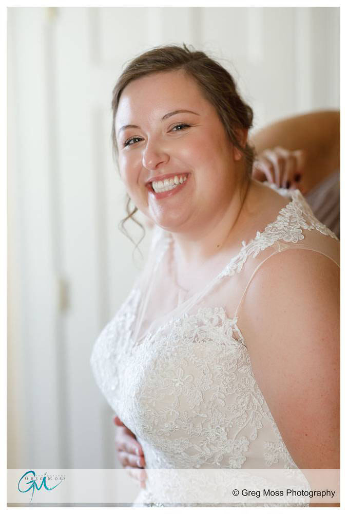 Bride smiling while maid of honor buttons up the dress.