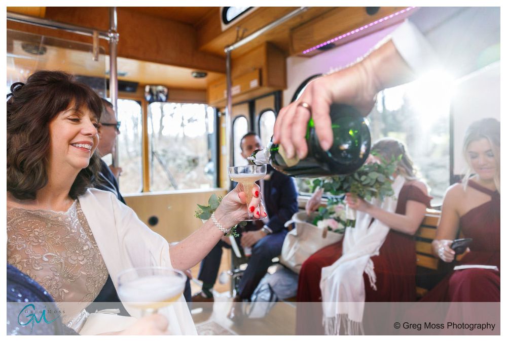 Groom filling mom's champagne glass on their ride on the trolley to the mansion on bald hill