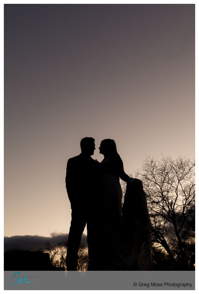 a silhouette of the bride and groom standing on ledge with the bride holding her train