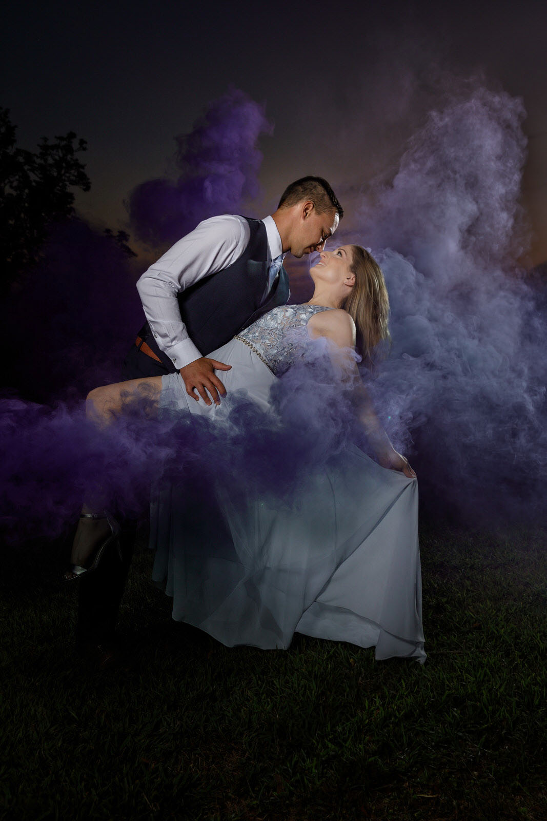 Elegantly dressed couple dipping at sunset with purple smoke. With engagement photo shoot tips