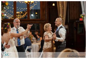 A wedding reception inside the Red Barn at Hampshire College with two couples dancing joyfully, lights twinkling in the background.