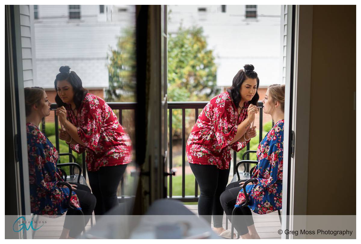 Publick house vov renewal 001 Two women applying makeup in front of a mirror, reflected in a glass door leading to a balcony, with a Publick House Vow Renewal logo watermark in the corner.