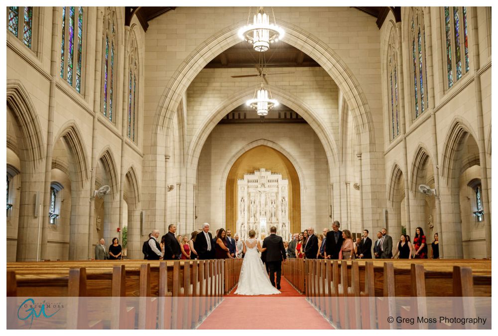 Log Cabin Holyoke Weddings-14 A wedding ceremony inside a log cabin with a couple standing at the altar, surrounded by guests seated under arched ceilings and stained-glass windows.