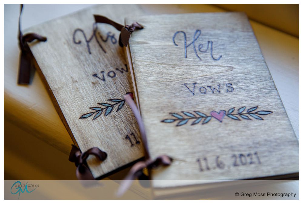 Inn on Boltwood Fall wedding-1 Two wooden wedding vow books with engraved titles and a date, "7.16.2021", decorated with leaves and a heart, captured at the Inn on Boltwood during a fall wedding, lying