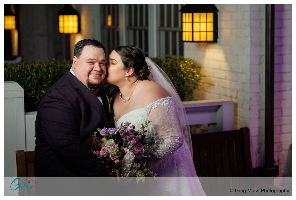 Inn on Boltwood Fall wedding-17 A bride and groom embracing and kissing outdoors at the Inn on Boltwood, with the bride holding a bouquet of flowers.