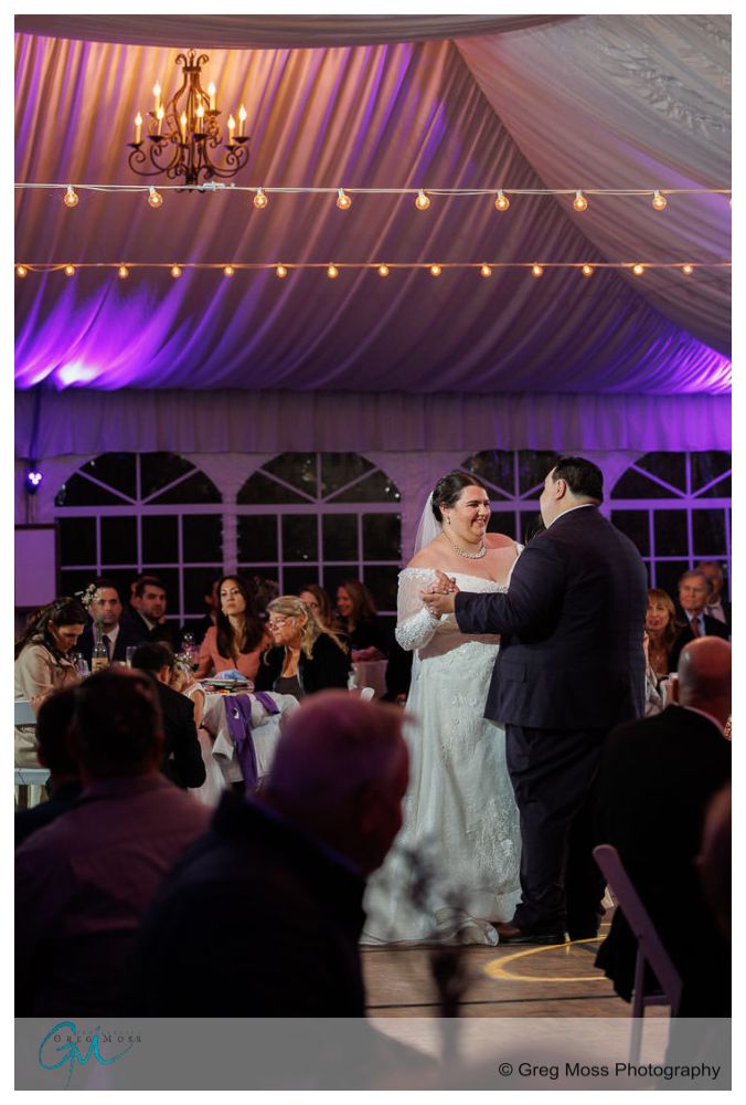 Inn on Boltwood Fall wedding-19 Bride and groom share their first dance under a tent with purple lighting at the Inn on Boltwood, surrounded by seated guests watching them.