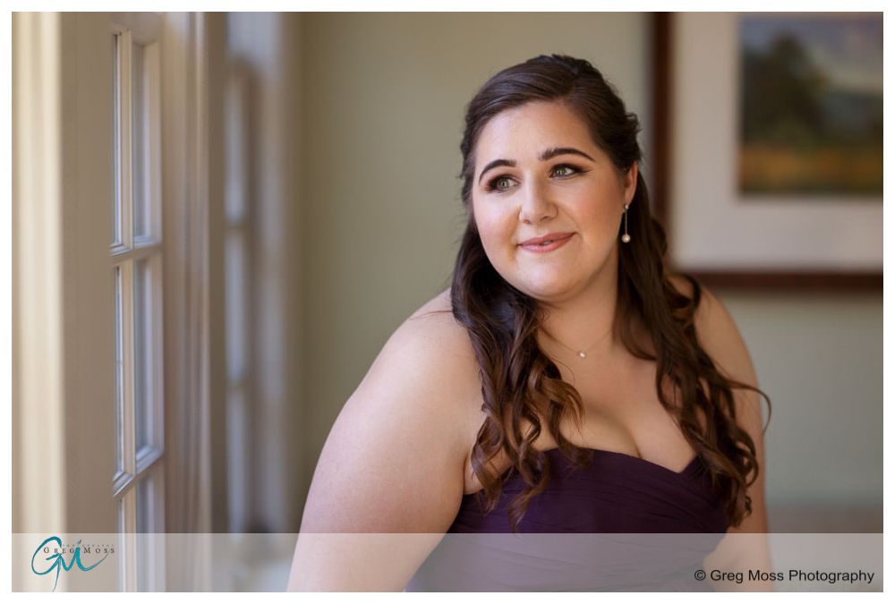 Inn on Boltwood Fall wedding-2 A woman in a purple dress smiling gently while looking out a window at an Inn on Boltwood Fall Wedding, photographed in a softly lit room.