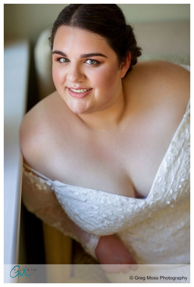 Inn on Boltwood Fall wedding-5 A young woman in a bridal dress poses smiling at the camera, partially wrapped in a sheer fabric, near a window at an Inn on Boltwood fall wedding.