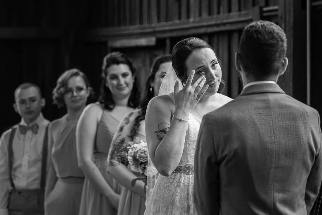 Red Barn Wedding Photography-14 Black and White photo of bride wiping a tear away during ceremony
