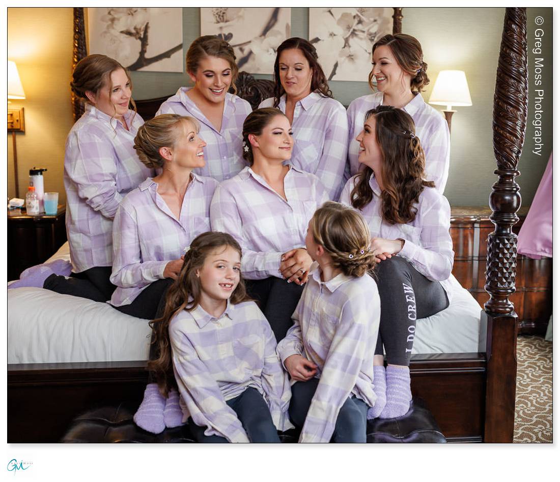 Holyoke Wedding Photography-2 Group of women and girls in matching plaid pajamas smiling and posing together on a bed in a well-decorated room, captured by Holyoke Wedding Photography.