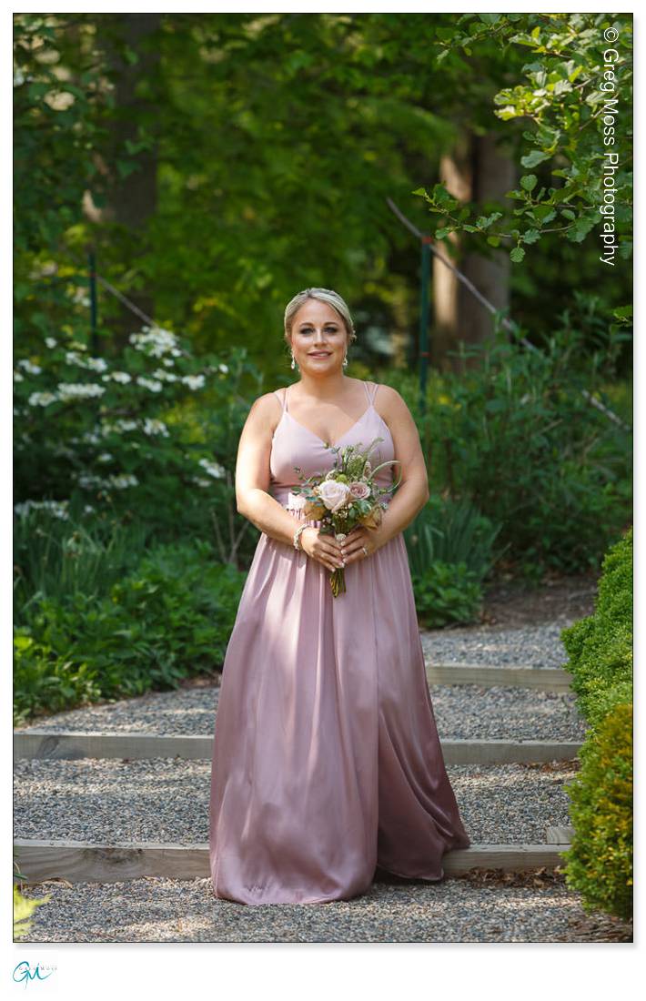Highfield Hall Wedding-15 Woman in a blush pink gown holding a bouquet, standing on a stone pathway at Highfield Hall Wedding.