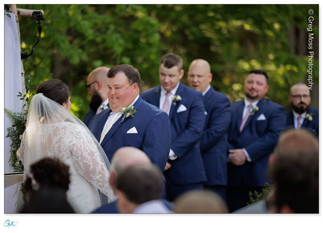 Highfield Hall Wedding-17 Bride and groom standing at the altar during a Highfield Hall wedding ceremony, with the groom looking at the bride affectionately, surrounded by groomsmen in blue suits.