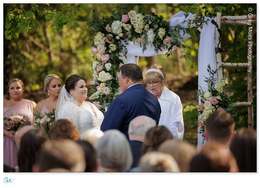 Highfield Hall Wedding-18 A bride and groom exchange vows at a Highfield Hall wedding ceremony, with a floral arch and guests watching in the background.