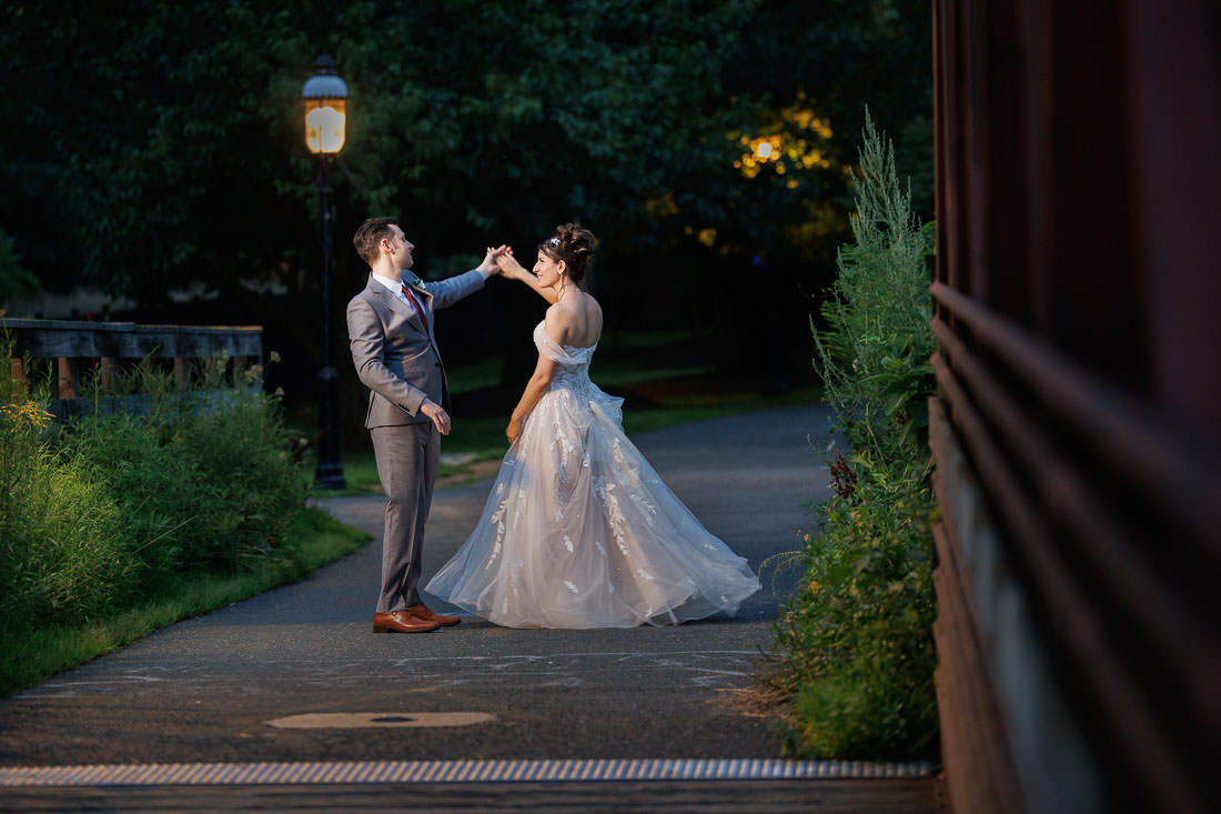 Union Station Wedding-18 Briana and Jacob, a newlywed couple, share a romantic moment on a path at twilight during their Union Station Wedding in Northampton, MA, with the groom lifting the bride's hand as