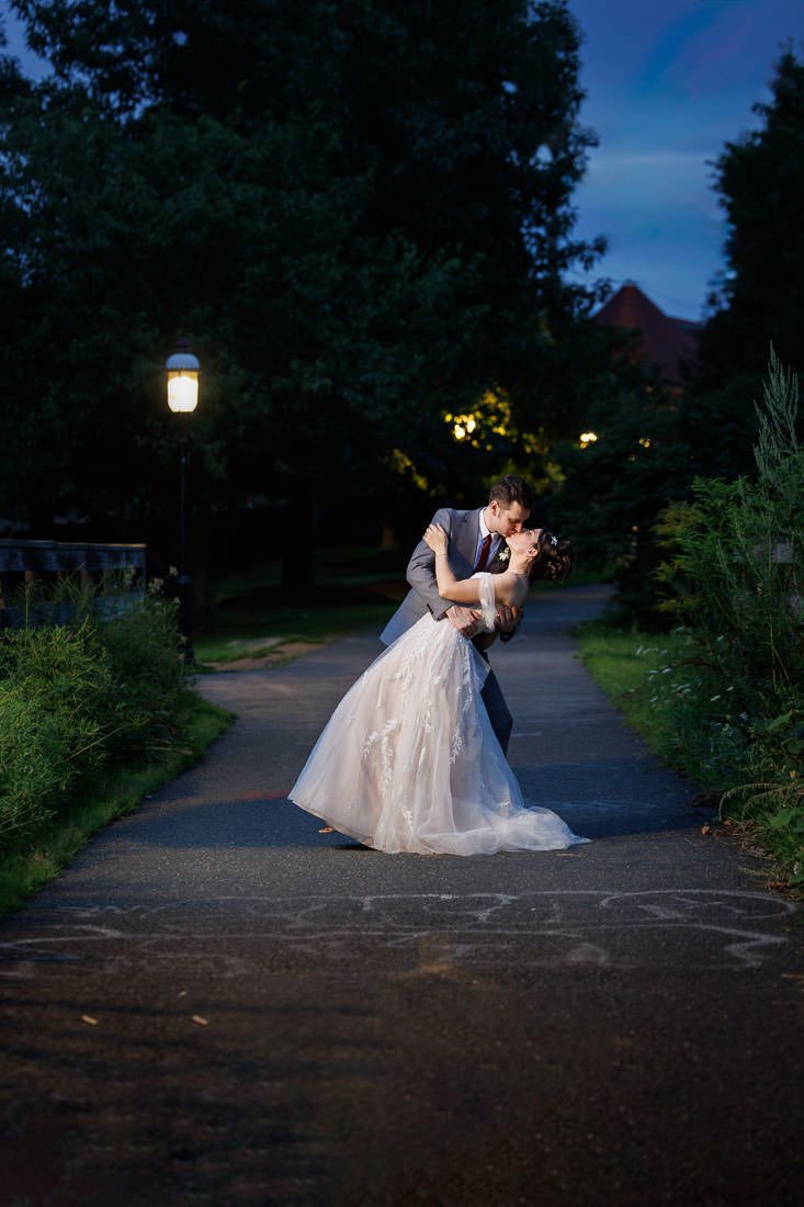 Union Station Wedding-19 Briana and Jacob share a romantic kiss on a lamplit park path at dusk, the bride's flowing gown and the groom's suit highlighted in the soft evening light.