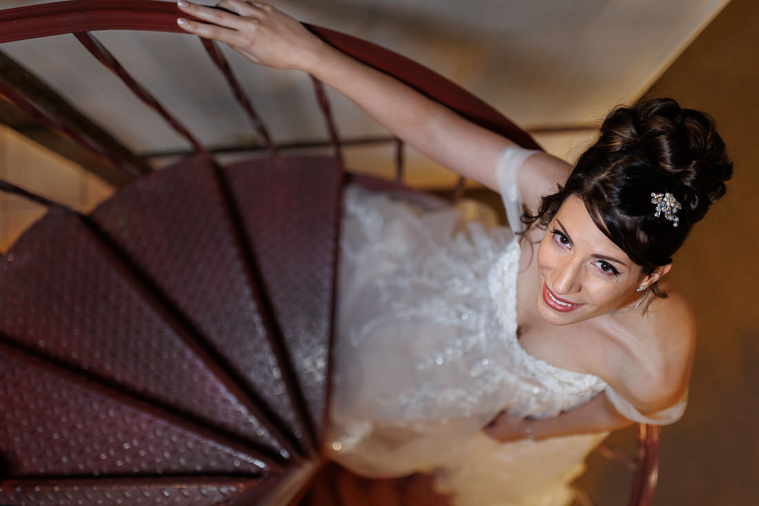 Union Station Wedding-3 A bride in a white dress smiles while ascending a spiral staircase at Union Station, viewed from above.