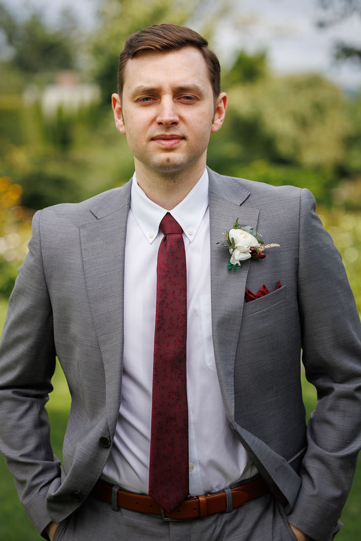 Union Station Wedding-4 Man in a gray suit and red tie with a boutonniere, standing in a garden at Union Station Wedding.