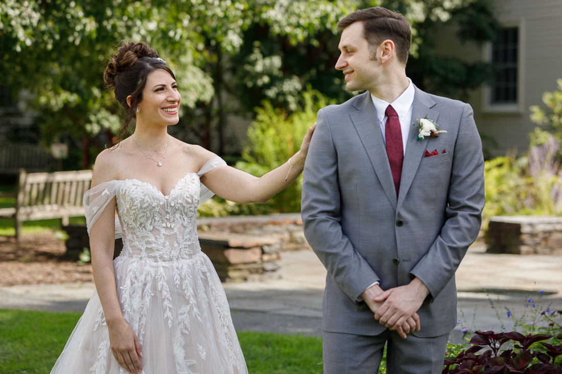 Union Station Wedding-5 Bride Briana in a white gown smiling at groom Jacob in a grey suit as she touches his chest in a garden setting at Union Station Wedding, Northampton Ma.