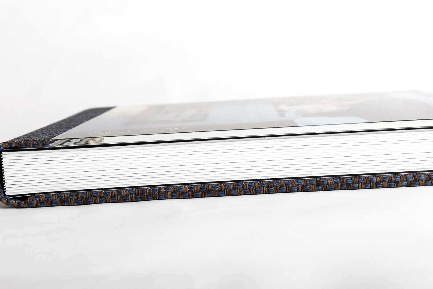 Side view of a closed wedding album with a thick stack of white pages and a decorative blue and gold patterned binding, against a white background.