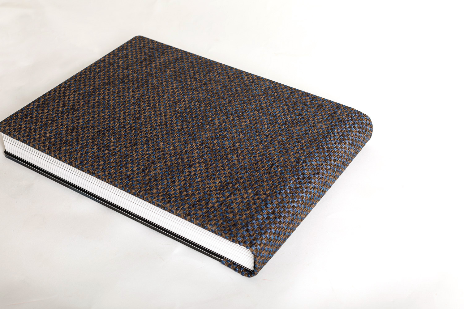 A closed wedding album with a textured blue and brown cover resting on a white surface.