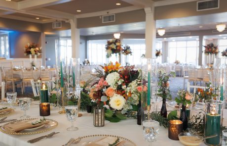 An elegantly set banquet table with floral centerpieces and candles in a spacious, well-lit hall, ready for an event.