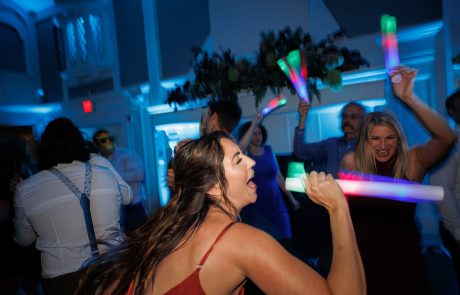 People are dancing and waving colorful light sticks in a dimly lit room with blue lighting.
