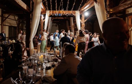 People dancing under string lights in a dimly lit, rustic venue with tables and seated guests in the foreground.