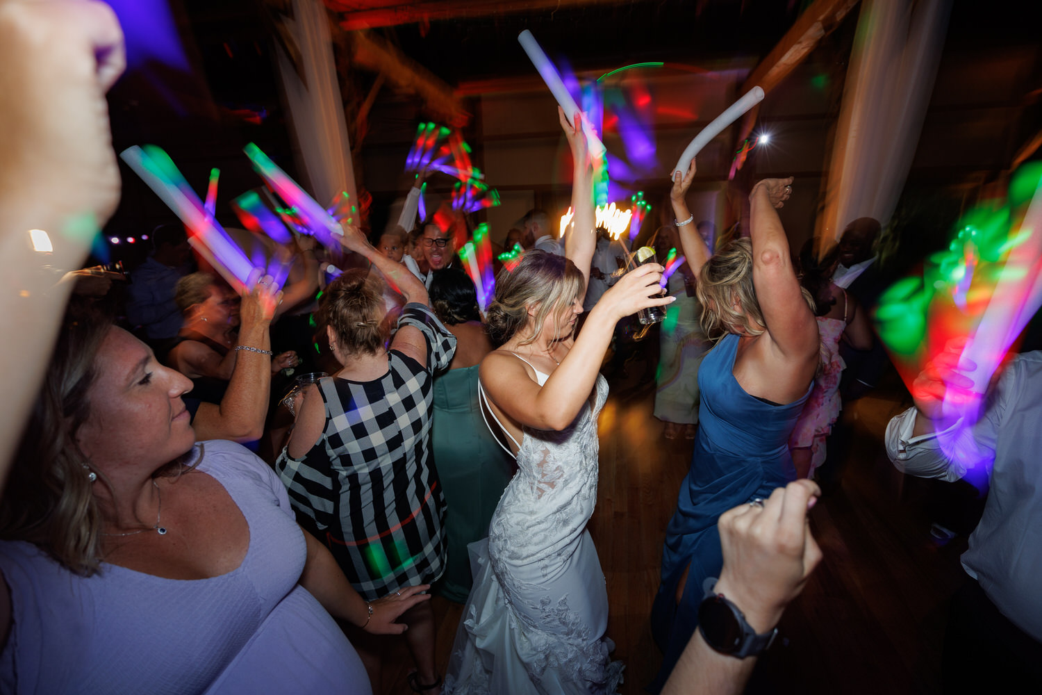 People dancing energetically with glow sticks at a lively indoor party or event, illuminated by colorful lights.