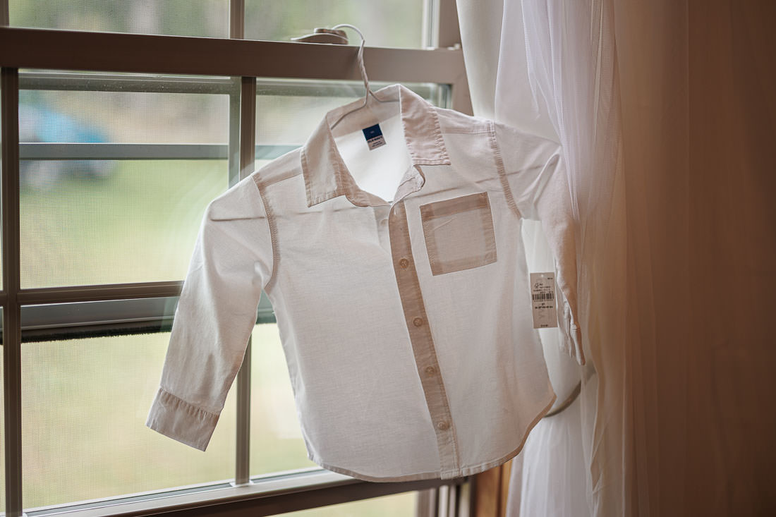 Bliss Farm Wedding-2 A white long-sleeve button-up shirt on a hanger gently sways by the window, where soft light reminiscent of Crestview Country Club wedding photos streams through.