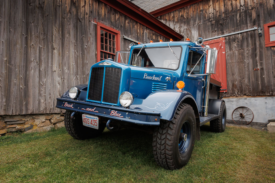 Bliss Farm Wedding-5 A vintage blue truck parked on grass in front of a weathered wooden barn with red-trimmed windows and doors creates the perfect rustic backdrop, reminiscent of charming Crestview Country Club wedding photos.