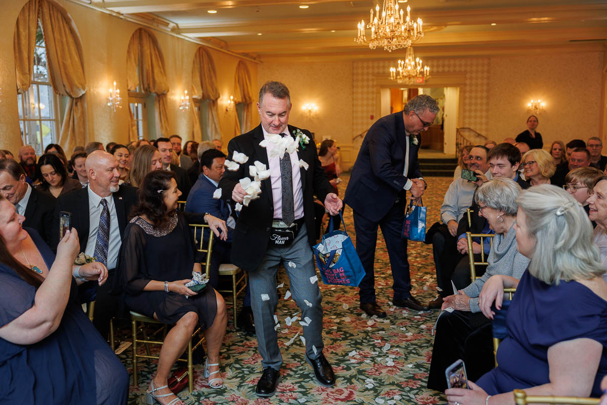 Hotel Northampton Wedding-18 At The Northampton Hotel wedding, a man walks down an aisle, gracefully tossing flower petals while guests seated on both sides watch and smile.