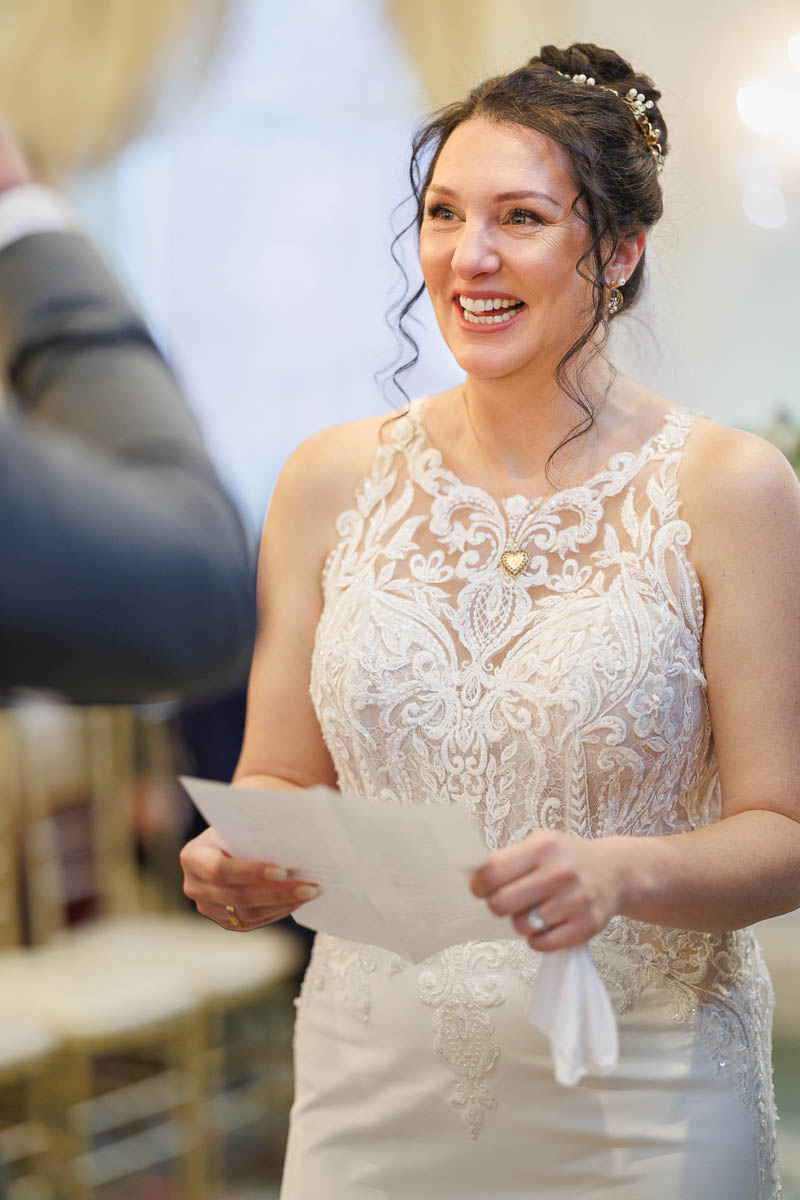 Hotel Northampton Wedding-21 A woman in a lace wedding dress beams while holding a paper, with chairs set up in the background at The Northampton Hotel Wedding.