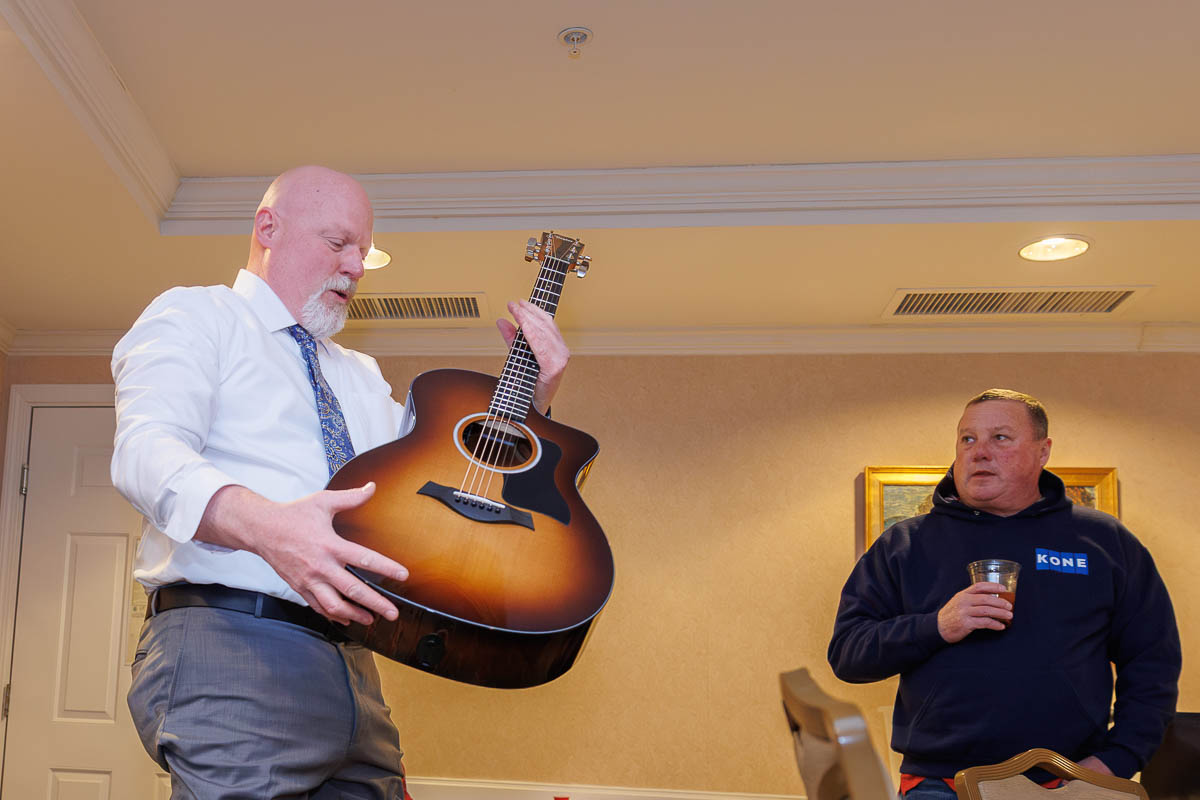 Hotel Northampton Wedding-6 In the cozy room of The Northampton Hotel Wedding, a man in a tie cradles an acoustic guitar while another in a hoodie sips his drink nearby.