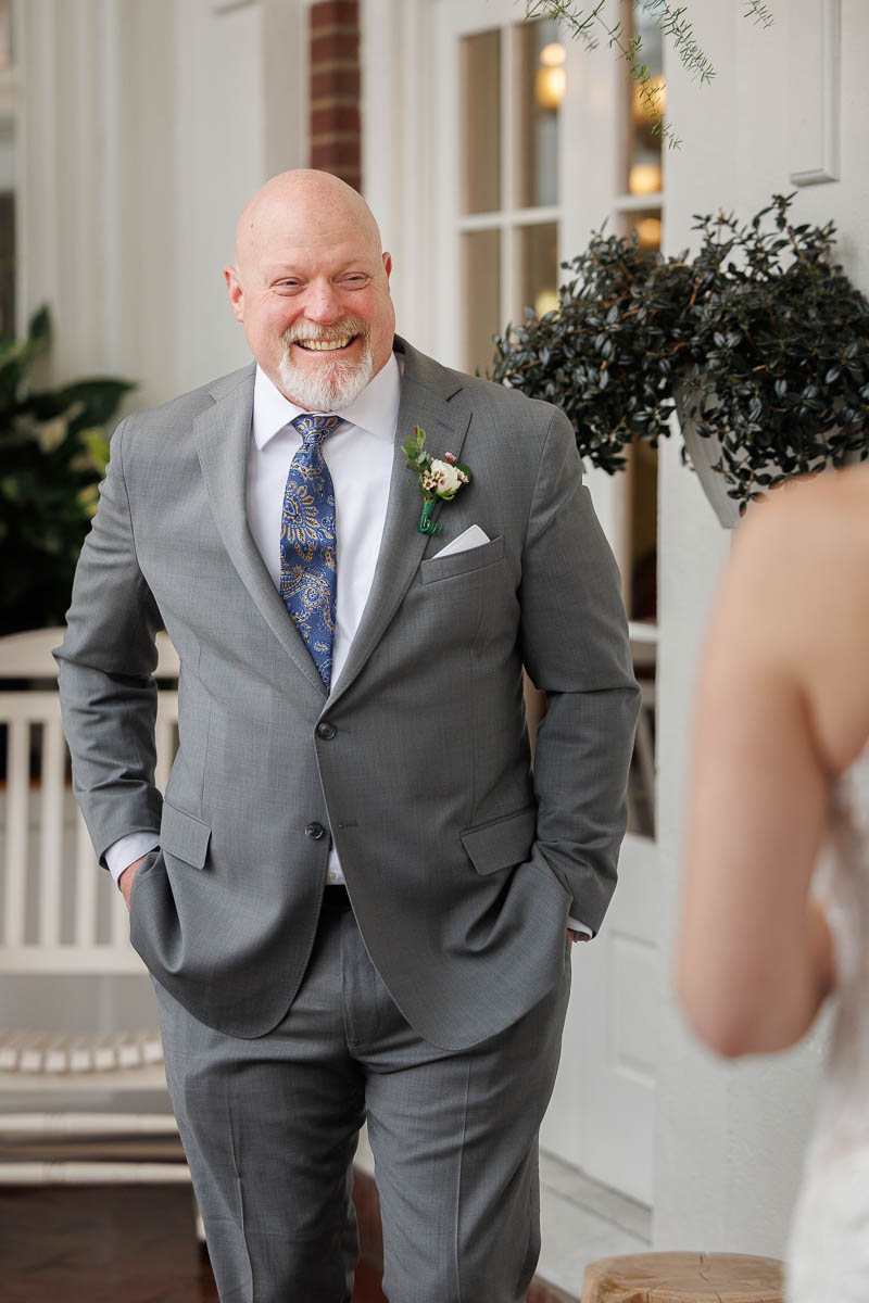 Hotel Northampton Wedding-9 A man in a gray suit with a floral boutonniere smiles warmly at the person in the wedding dress, their moment captured beautifully indoors at The Northampton Hotel Wedding.
