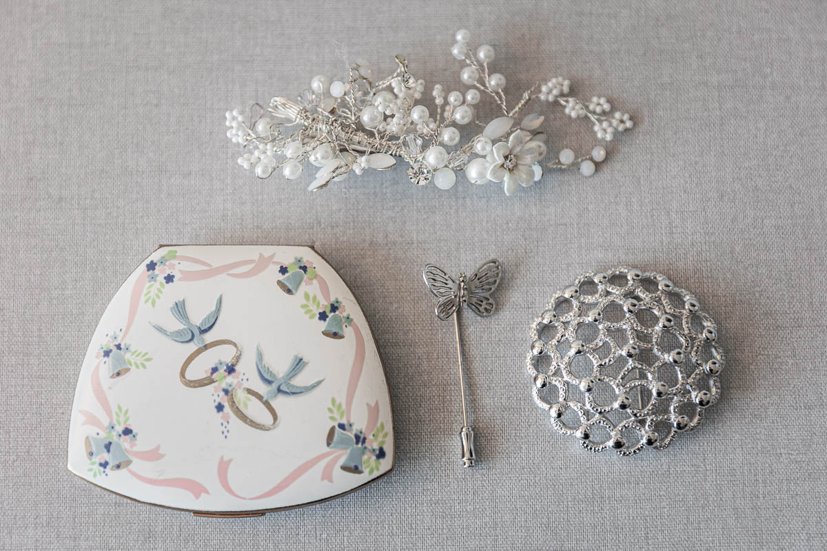 Maneeley’s banquet wedding-1 A floral headpiece, vintage butterfly hairpin, and decorative silver brooch elegantly capture the essence of Maneeley's Ct Winter Wedding Photos as they are arranged on a gray surface along with a compact case adorned with birds and rings.