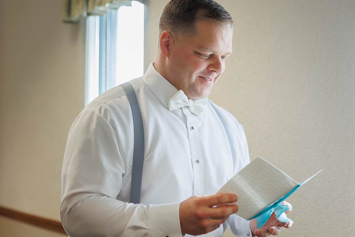 Maneeley’s banquet wedding-11 By a window at Maneeley's Ct, where winter wedding photos capture countless memories, a person in a white shirt and bow tie reads a letter, smiling gently.