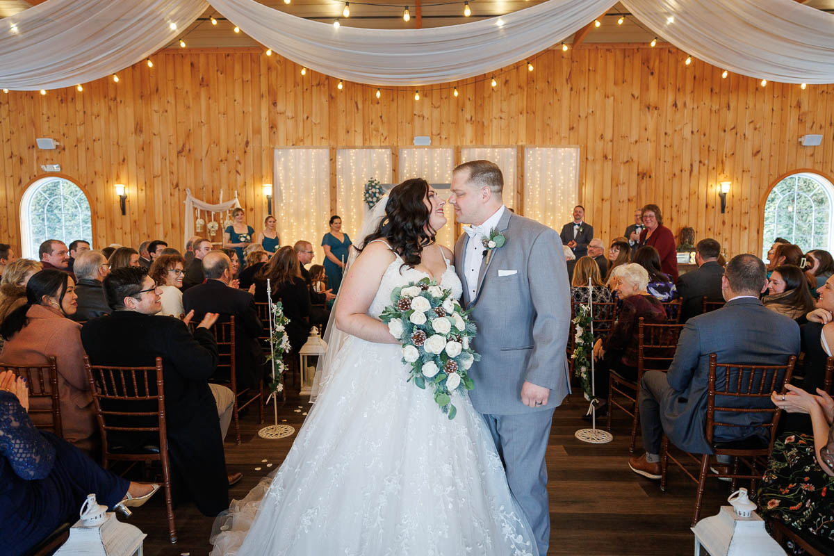 Maneeley’s banquet wedding-16 The bride and groom share a kiss in the beautifully decorated wooden hall at Maneeley's Ct, surrounded by seated guests, capturing the warmth and charm of winter wedding photos.