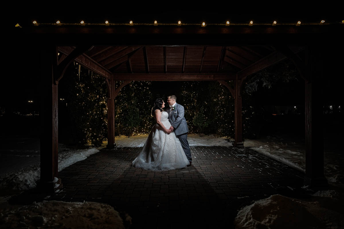 Maneeley’s banquet wedding-23 The bride and groom stand under a gazebo at night, surrounded by shimmering lights and gentle snow, creating magical Maneeley's Ct Winter Wedding Photos.