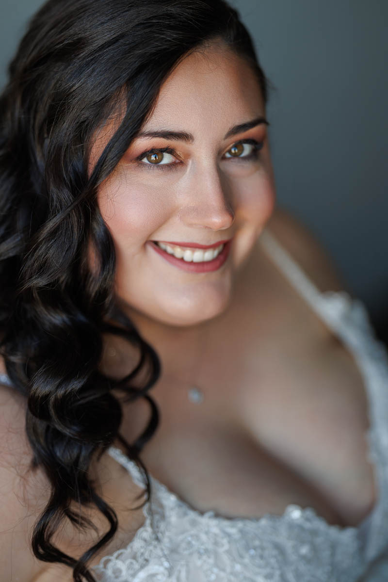 Maneeley’s banquet wedding-7 A person with long, dark wavy hair smiles at the camera, wearing a white garment with lace details, reminiscent of elegant winter wedding photos at Maneeley's.