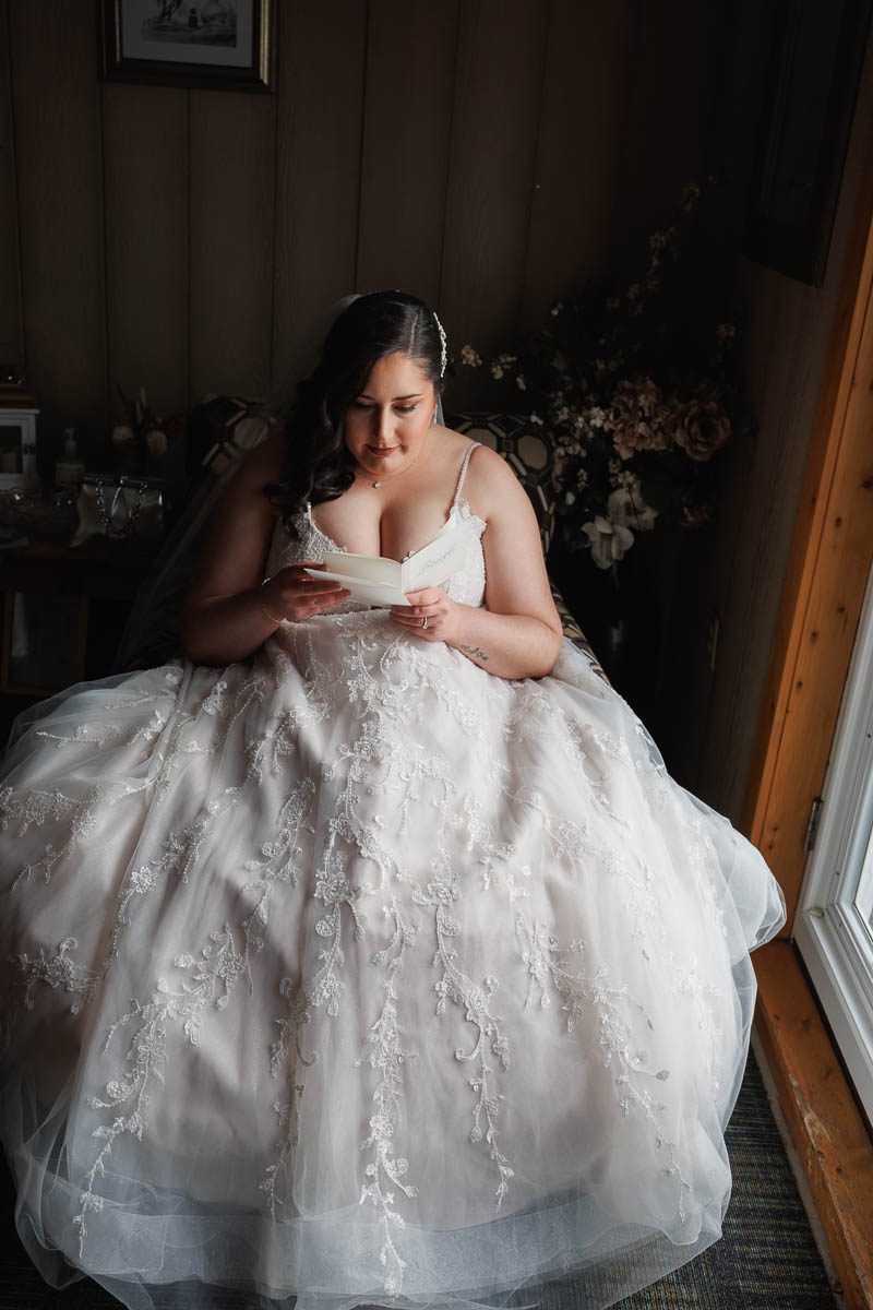 Maneeley’s banquet wedding-9 A bride in a lace wedding dress sits by a window at Maneeley's Ct, savoring a heartfelt note. The essence of winter wedding photos captures this intimate moment beautifully.