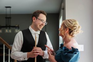 A man in formal wear holding a pool cue smiles at a woman in an off-shoulder dress as they talk in a well-lit room, capturing the charm of The Ranch Wedding Photo style.