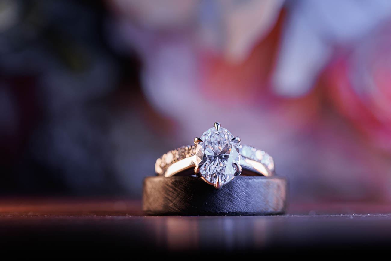 The Ranch Wedding photos-22 A diamond engagement ring and a wedding band are placed together on a reflective surface, with a blurred, colorful background capturing the magic of The Ranch Wedding Photo.