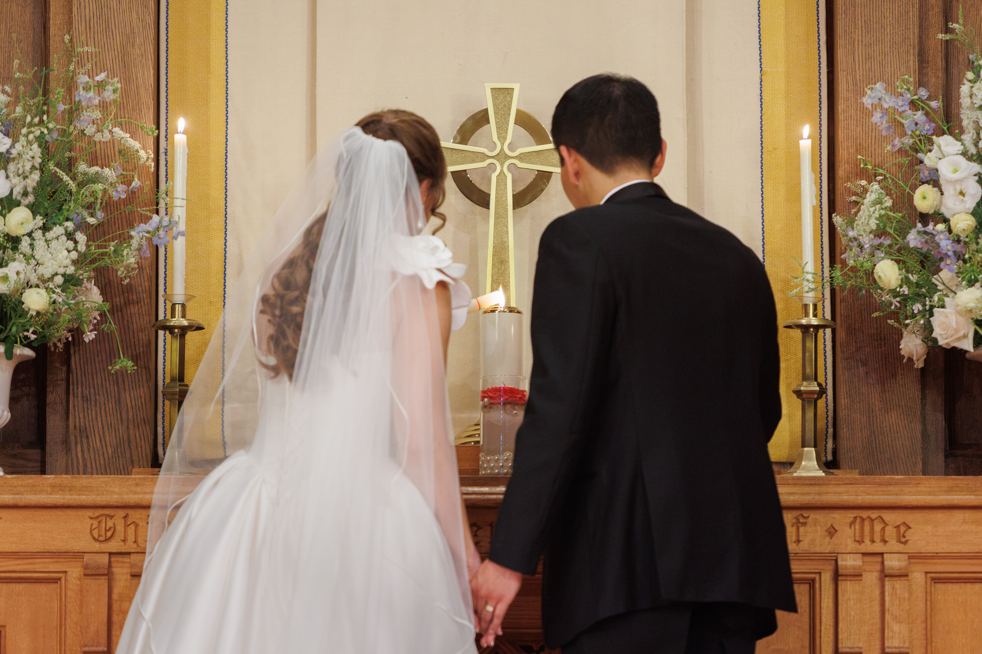 Natasha and Fang-373 Lyman Estate Wedding A bride and groom stand at an altar with lit candles and elegant floral arrangements, facing a cross during their Lyman Estates Wedding ceremony.