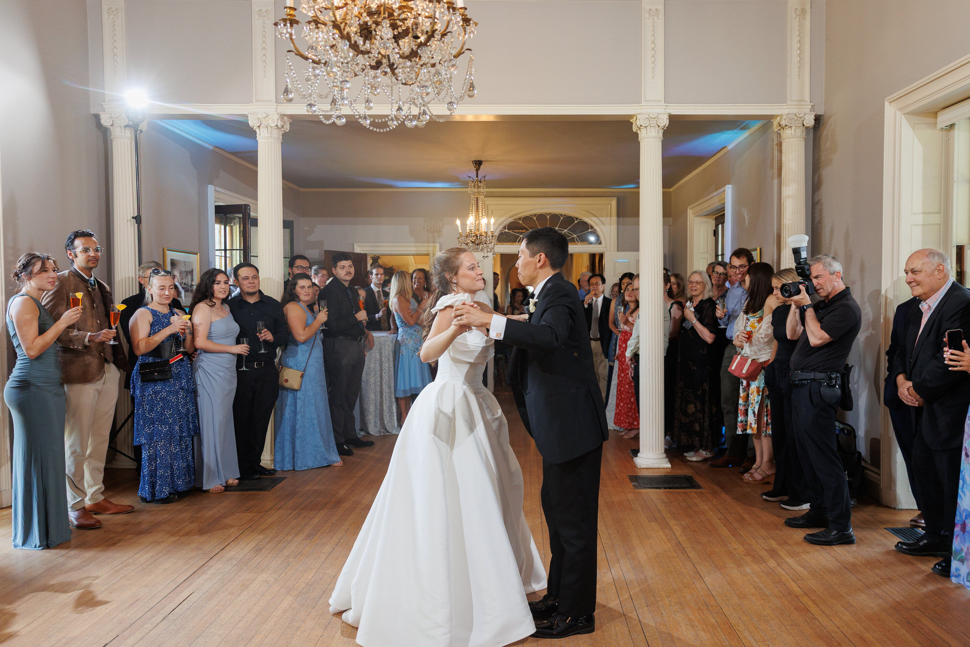 Natasha and Fang-458 Lyman Estate Wedding A bride and groom share their first dance in a beautiful ballroom at their Lyman Estates wedding, surrounded by guests watching and taking photos.